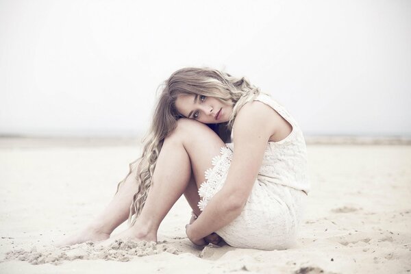 Lisa dans une robe blanche et avec un regard triste sur le sable