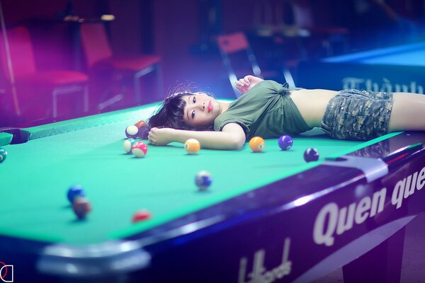 A girl on a table among billiard balls