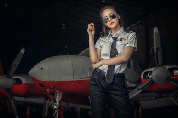 A girl on the background of an airplane in a pilot s uniform and sunglasses