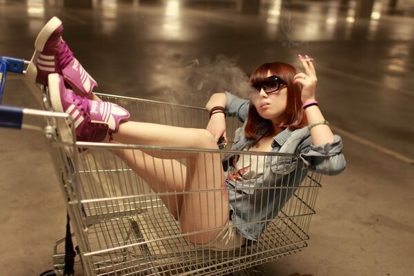 Chica asiática se sienta en la cesta de la compra