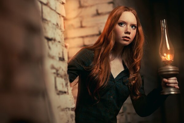 Red-haired girl with a lamp in a dark place