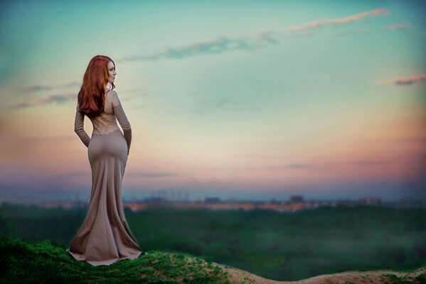 A red-haired slender woman in an evening dress against the sunset