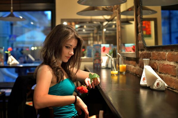 Chica sentada en un Bar con una rosa en la mano