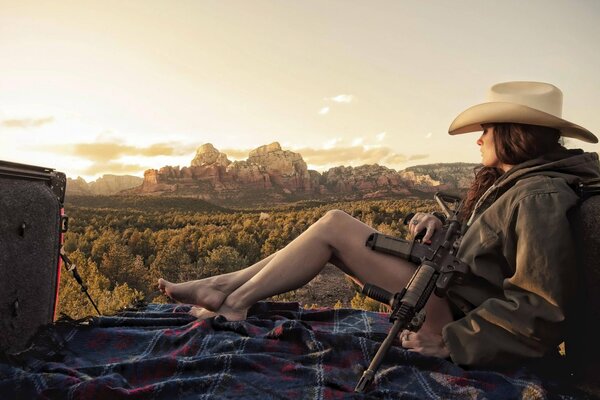 A brunette girl in a pickup truck is holding a rifle. Looks at the mountains