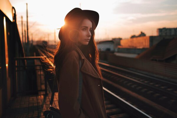 Portrait of a girl in a hat on the railroad during sunset