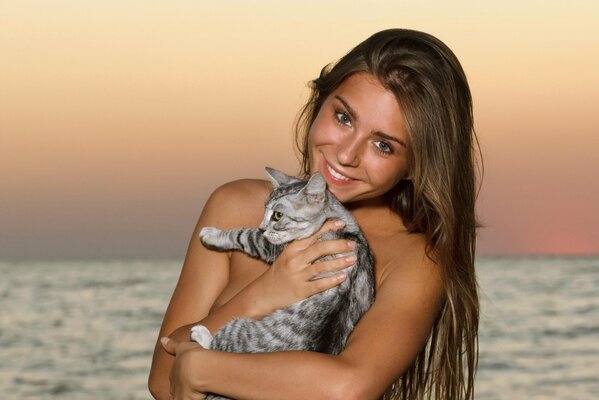 Long-haired smiling girl with a cat on the background of the sea