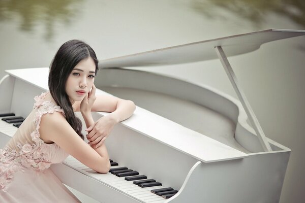 Chica asiática se sienta en el piano junto al agua