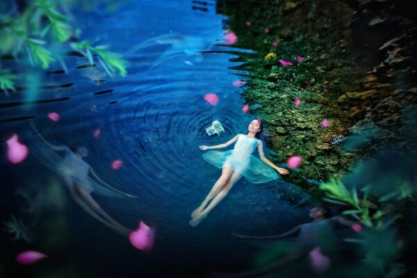 A girl lying in the water against a background of green grass and flowers