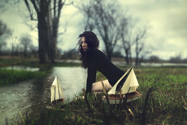 A girl in a black dress launches boats on the river