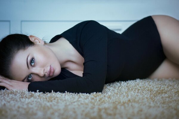 A beautiful girl in a black bodysuit is lying on the carpet