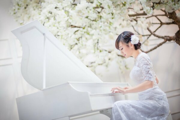 Ragazza asiatica in abito bianco suona un pianoforte bianco su sfondo bianco