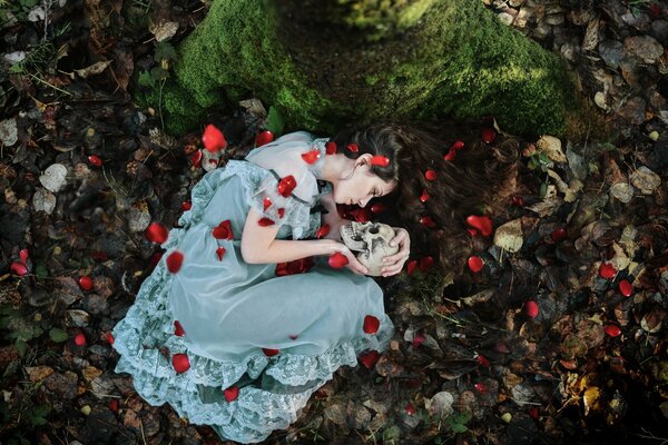 A girl lies with a skull on rose petals