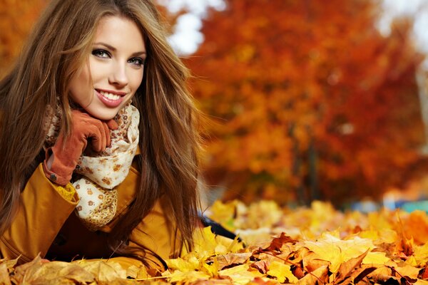 A beautiful girl is smiling. A young girl on the background of an autumn landscape. The girl is lying on golden autumn leaves