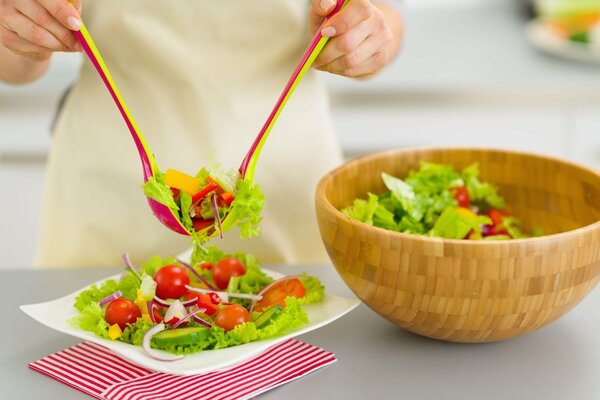 Las manos ponen una ensalada verde en un plato