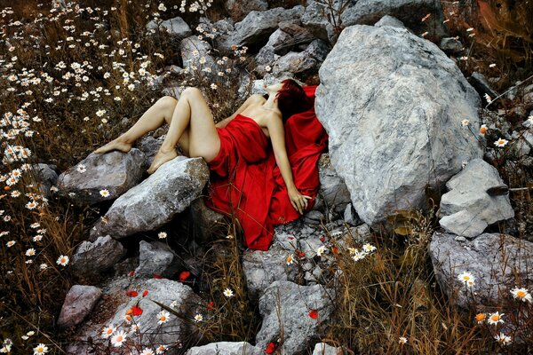 Professionelles Foto des Mädchens im roten Kleid. In einem roten Kleid auf einem Hintergrund von Steinen