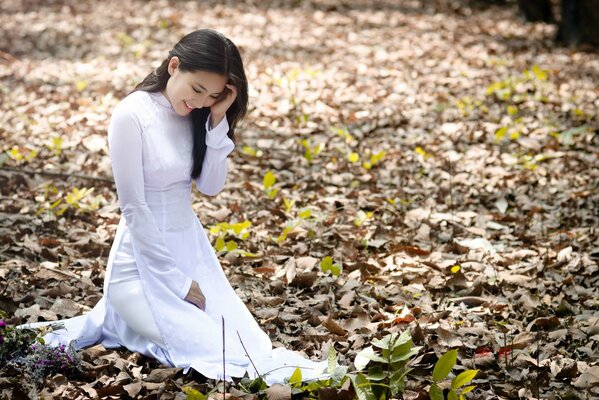 Chica con vestido blanco de pie en las hojas de otoño