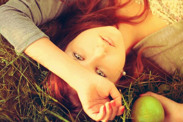 Photo thématique. Fille aux cheveux roux dans les pommes. Tendre fille se trouve sur l herbe