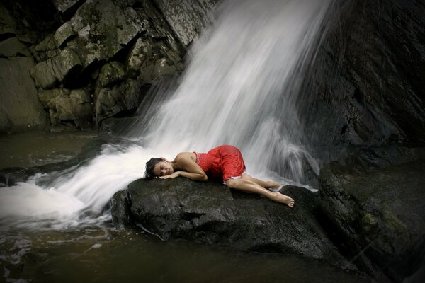 A girl in a red dress under a waterfall