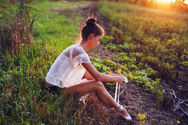 A girl in the evening in nature tightens pointe shoes