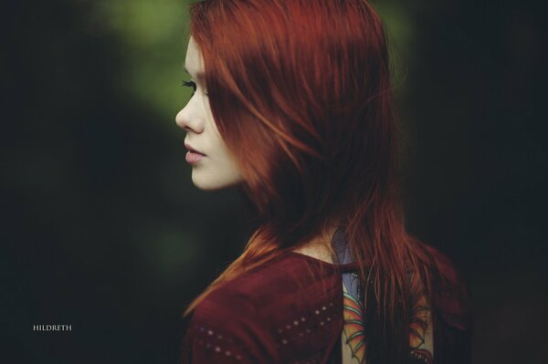 A red-haired girl stands with her back to the photographer