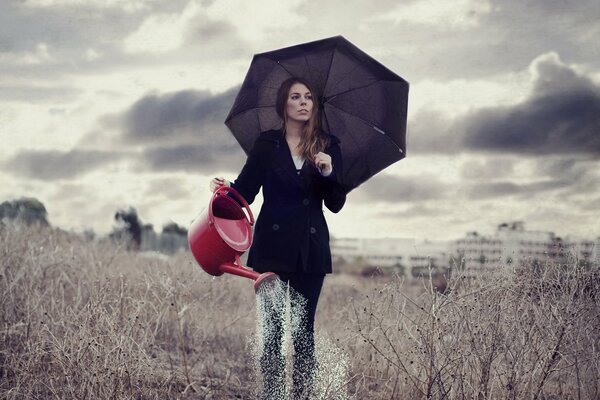 A girl under an umbrella pours from a watering can