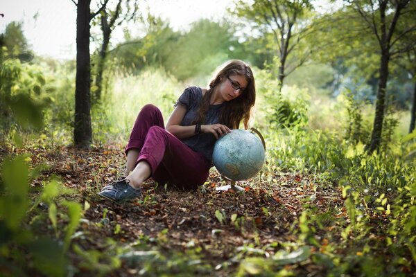 A girl with a globe on the background of a forest