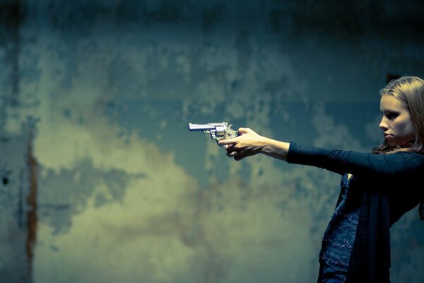 Chica con una pistola en la mano, en el fondo de la pared