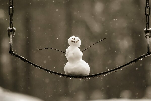 UN MUÑECO DE NIEVE SE BALANCEA EN UN COLUMPIO EN INVIERNO