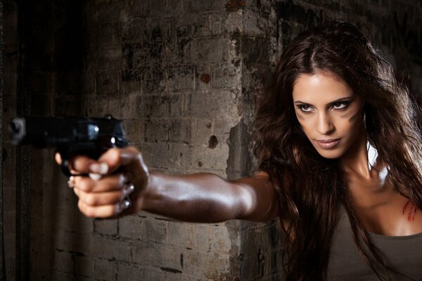 Chica con una pistola en la mano, contra una pared de fondo