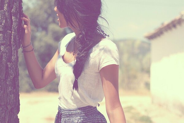 Brunette with her back. Summer photo in soft colors. The girl near the tree