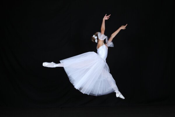 A ballerina s leap in a white dress on a black background