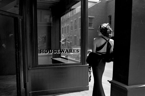 Foto en blanco y negro de una niña con la espalda cerca de la vitrina
