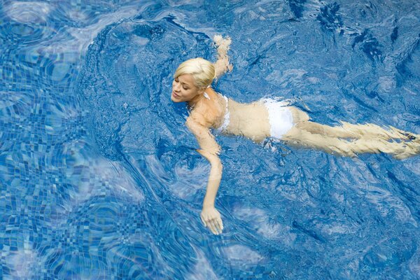 Ragazza bionda in costume da bagno bianco nuota in acqua