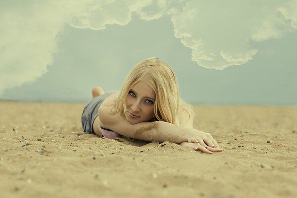 Blondine im Sand unter den Wolken