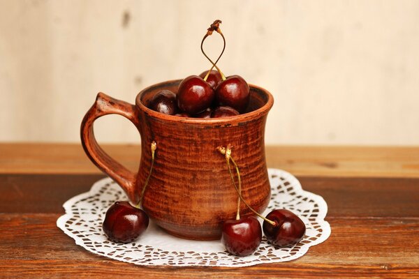 Cherries in a clay mug on a white lace napkin