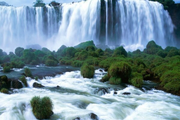 Ein stürmischer Wasserfall, der in den Fluss übergeht, inmitten des Grüns