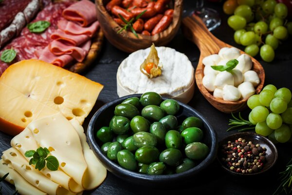 An appetizing table with snacks in the form of various cheeses, fruits, ham and olives