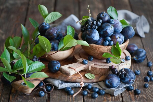 Stillleben aus Pflaumen und Blaubeeren auf Holzgeschirr