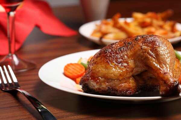 Sur la table se trouve une assiette de poulet et à côté d une fourchette avec un verre