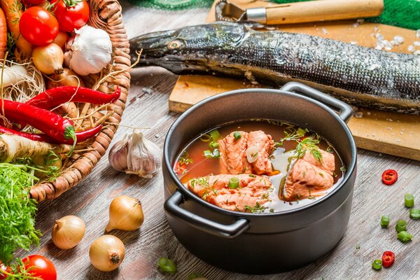 Ohr in einem Topf auf einem Fischhintergrund auf einem Schneidebrett und einem Korb mit Gemüse