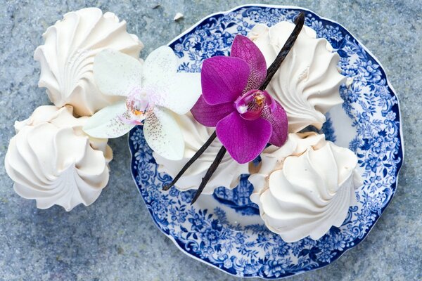 Süßes Dessert aus weißem Marshmallow auf einem blauen Teller mit einer schönen rosa Orchidee