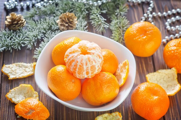 Winterurlaub. Orangefarbene Zitrusfrüchte auf einem Teller. Umgeben von Rinde und Fichte