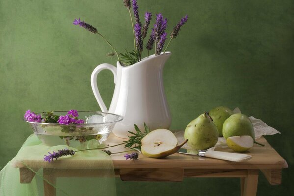 A jug of lavender on a wooden table with pears