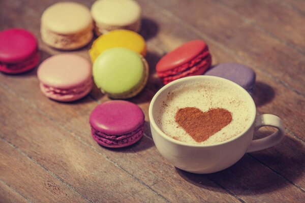 Macaroons on the table next to cream coffee in a foam mug with a heart on it