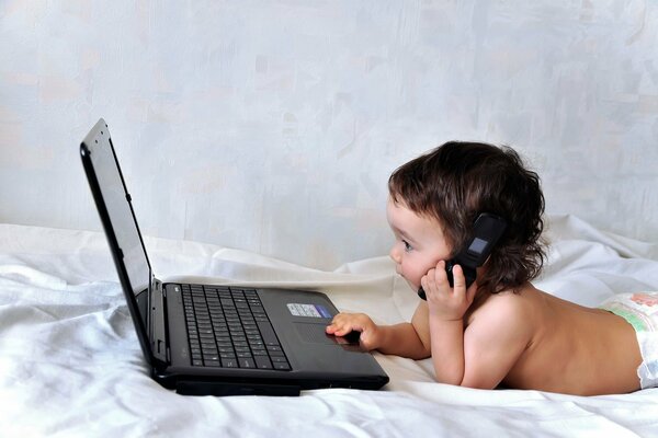 Un niño pequeño detrás de una computadora portátil con un Teléfono