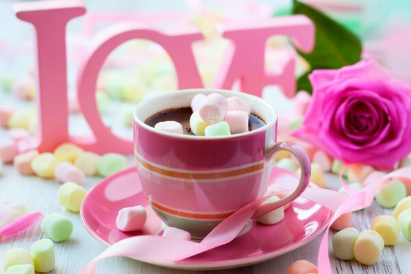 A cup of hot chocolate with marshmallows on the background of a rose and the inscription love