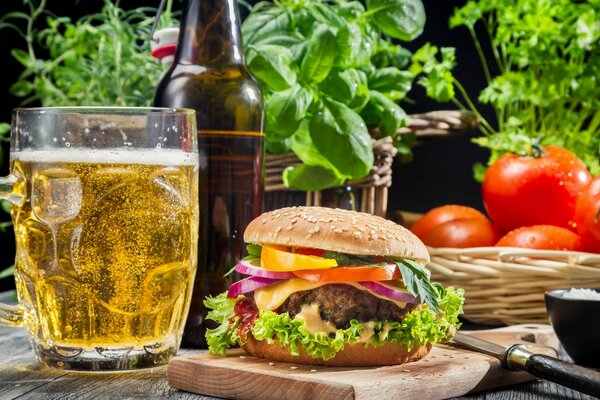 A glass of beer , a burger , tomatoes and greens on the table