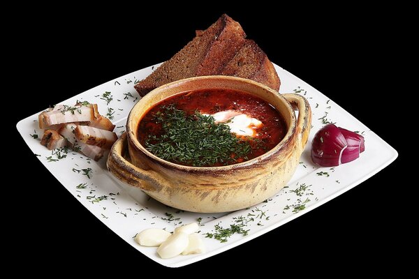 A plate of borscht with bread bacon and garlic