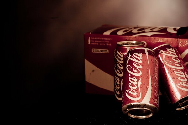 Three cans of Coca Cola next to the box