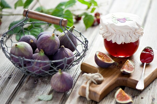 Figs in a basket next to a jar of jam on a wooden board